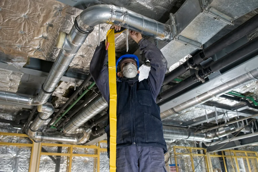 Professional installer sealing overhead sheet metal ductwork during a ventilation project in Ontario.