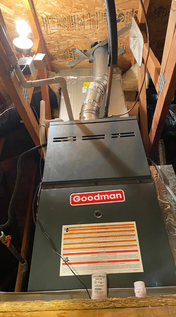 A vertical Goodman gas furnace system with metal exhaust venting installed inside a residential attic space.