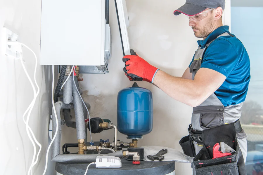 Technician inspecting a wall mounted water heating system and blue expansion tank in San Bernardino.