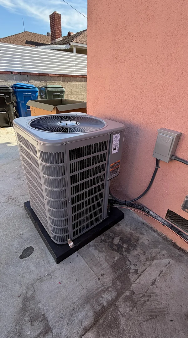 A residential outdoor air conditioning unit installed against a peach stucco wall in Fullerton.