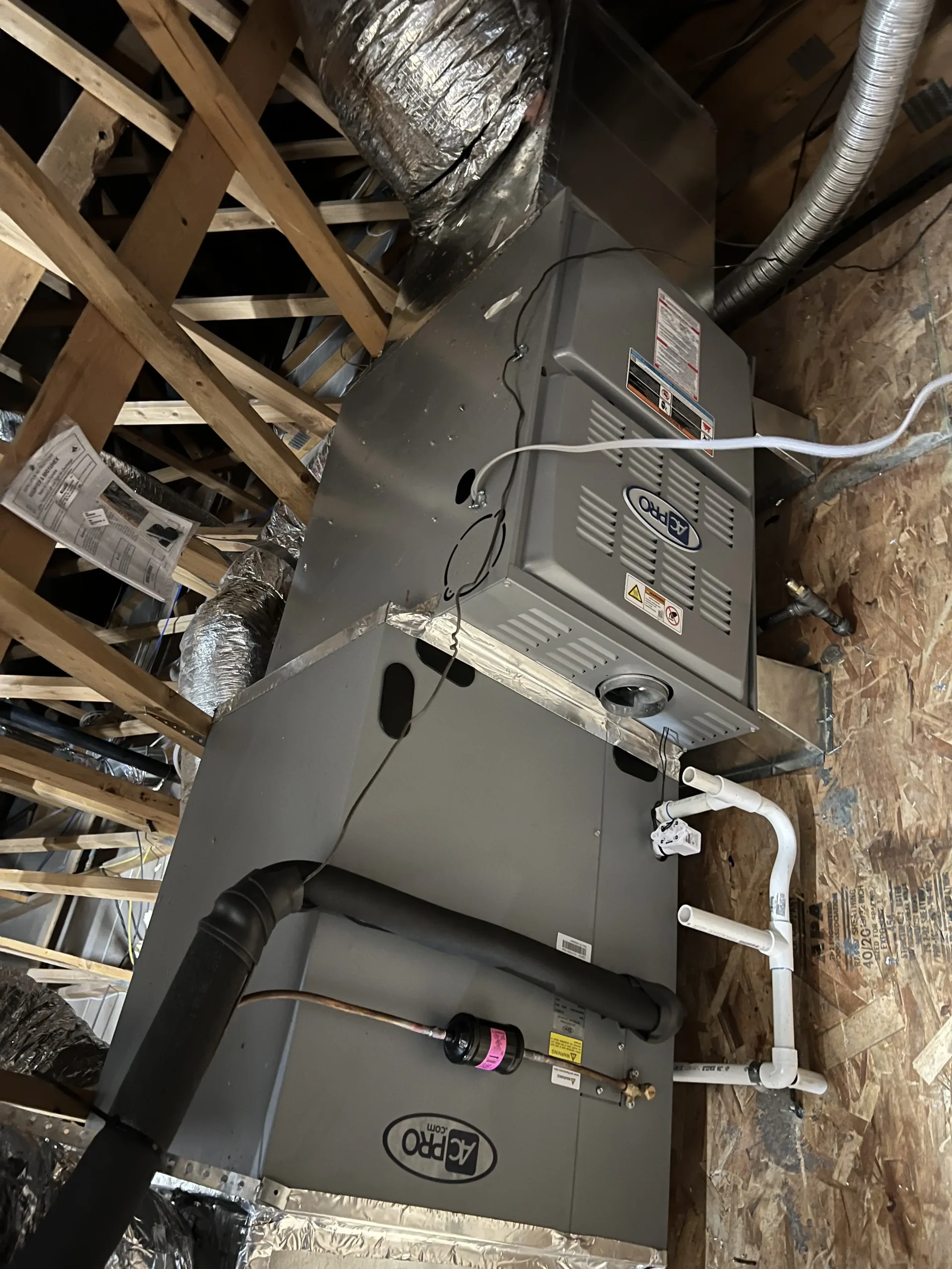 An AC Pro heating and cooling system with silver flexible ductwork mounted inside an unfinished wooden attic.
