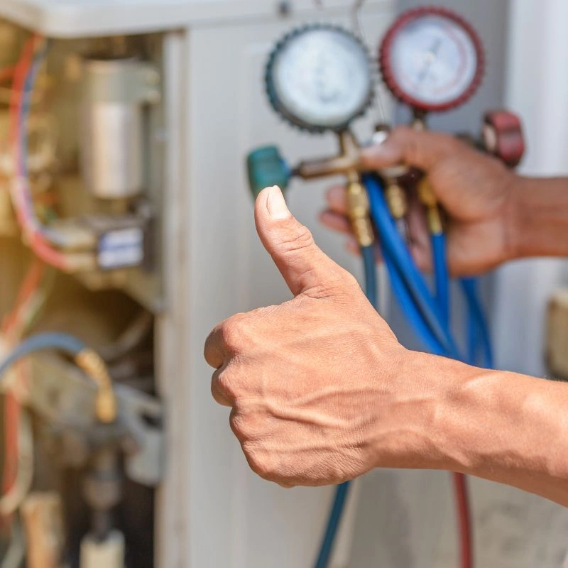 An HVAC specialist giving a thumbs up gesture while carrying diagnostic manifold gauge hoses during an AC tune up.