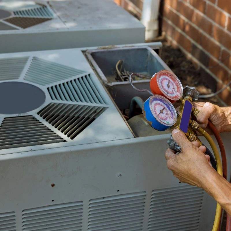 A professional technician connecting manifold pressure gauges to a backyard condenser during air conditioning maintenance.