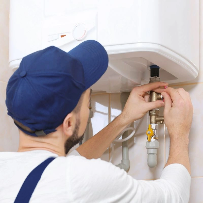 An HVAC professional carefully adjusting a brass pressure valve below a white wall-mounted boiler system.
