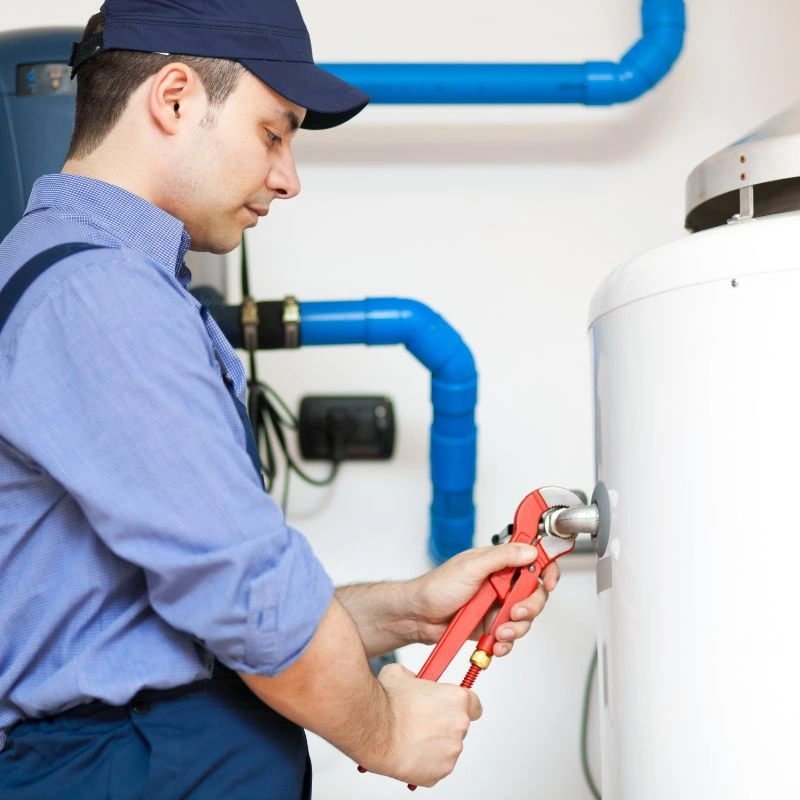 A professional service technician using a red pipe wrench to secure plumbing connections on a large white tank.
